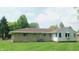 Well-maintained backyard featuring a stone exterior, manicured lawn, and lush trees at 7326 Lowe Dr, Lawrence, IN 46226