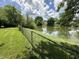 View of the backyard and pond surrounded by lush greenery and a black chain link fence at 7450 Cobblestone W Dr, Indianapolis, IN 46236