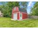 Red barn-style storage shed with a roll-up door, adding functional charm to the landscaped backyard at 1066 N Dogwood Way, Greenfield, IN 46140