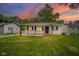 Charming single-story home featuring a covered porch and well-maintained landscaping against a dramatic sunset sky at 2035 W Kessler Blvd N Dr, Indianapolis, IN 46222