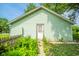Garage with light green siding and a white door, surrounded by green foliage and a sidewalk at 2627 Chase St, Anderson, IN 46016
