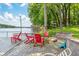 Inviting waterfront home features a spacious patio with vibrant red Adirondack chairs and a private dock on a sunny day at 6300 Grouse Dr, Nineveh, IN 46164