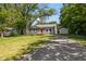 Charming single-story home with a red front door, gravel driveway, and detached garage surrounded by mature trees at 7424 North Dr, Lawrence, IN 46226