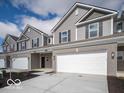 View of the townhome exteriors showing garages, gray siding, black shutters, brick accents and concrete driveways at 6304 Wasco Dr, Whitestown, IN 46075