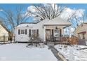 Charming white bungalow with covered porch and snow-covered yard at 5441 E 17Th St, Indianapolis, IN 46218