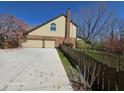 Side view of a home featuring a driveway leading to a garage, with a blooming tree and a wooden fence at 8429 Admirals Cv, Indianapolis, IN 46236