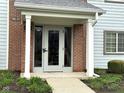 Close-up of covered entry to the home with red brick accent, columns, and well-maintained lawn at 8104 Glenwillow Ln # 208, Indianapolis, IN 46278