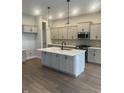 Open kitchen with large island, pendant lighting, stainless steel appliances, gray cabinets, and hardwood flooring at 525 Gilder Dr, Carmel, IN 46032