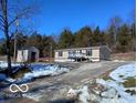 Tan mobile home with deck and storage building, snowy driveway and woods at 12160 W Baker Hollow Rd, Columbus, IN 47201