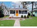 Single-story home with a well-manicured lawn and an inviting entrance with an orange door at 5630 Winthrop Ave, Indianapolis, IN 46220