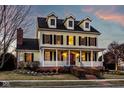 Charming two-story yellow home with a welcoming front porch and manicured landscaping at dusk at 12020 Leighton Ct, Carmel, IN 46032