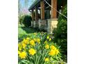 Close-up shot of a charming front porch, enhanced by yellow spring flowers, green bushes, and natural stone porch columns at 1307 W 161St St, Westfield, IN 46074