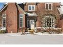 Close up of the front door and snow covered landscaping of a charming red brick home at 12978 Portsmouth Dr, Carmel, IN 46032