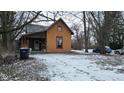 View of orange house with covered front porch and snowy yard with bare trees in winter at 1621 Indiana Ave, Anderson, IN 46012