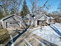 Charming gray home with an attached garage, beautiful landscape, and a driveway covered in snow at 717 Washington Ct, Anderson, IN 46011