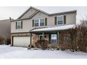View of two-story home showcasing a covered porch and two-car garage, with snow on the ground at 10991 Clear Spring Dr, Camby, IN 46113
