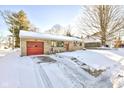 Ranch style home with a snow-covered front yard, stone siding, and a driveway leading to a red garage door at 115 N Spring St, Greenfield, IN 46140