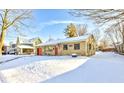 Side view of a single-story home featuring a red garage door, stone siding, snow-covered lawn, and mature trees at 115 N Spring St, Greenfield, IN 46140
