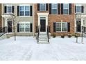 Close-up of a townhome exterior featuring brick and gray siding, black shutters, and a snow-covered lawn at 6965 Equality Blvd, Carmel, IN 46033