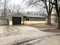 Well-maintained home with green siding, dark roof, and a paved driveway leading to an attached garage at 7824 Inverness Dr, Indianapolis, IN 46237