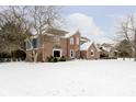 View of the side and back of this two-story home with brick facade and snowy yard at 13895 Silver Stream Dr, Carmel, IN 46032