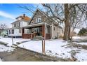 Charming two-story home featuring a welcoming front porch with brick accents and snow-covered yard at 2401 N Olney St, Indianapolis, IN 46218