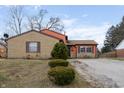 Charming split-level home featuring a brick and orange exterior, gravel driveway, and manicured shrubs at 3332 Ashway Dr, Indianapolis, IN 46224