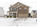Charming two-story home featuring brick and vinyl siding, attached garage and manicured landscaping on a snow covered lawn at 6413 Green Grass Ln, Whitestown, IN 46075