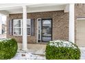 Inviting front porch with brick columns, decorative door with sidelight, and manicured bushes covered in snow at 6413 Green Grass Ln, Whitestown, IN 46075