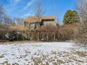 A weathered two-story house partially obscured by brush, with a brown roof in a snowy setting at 8676 W 1050 S, Fortville, IN 46040