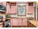 Charming kitchen featuring pink cabinets, wood countertops, stylish backsplash and modern stainless steel appliances at 1647 N Tacoma Ave, Indianapolis, IN 46218