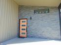Close-up of a modern, orange front door with sleek sidelights, complemented by the gray stone facade at 2528 Carrollton Ave, Indianapolis, IN 46205