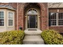Close-up of a brick entryway with a black front door, arched transom window, and manicured landscaping at 3880 Heathfield Ct, Zionsville, IN 46077