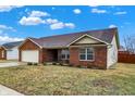 Classic brick ranch featuring an attached garage, and a manicured front lawn at 13 Watson Dr, Trafalgar, IN 46181