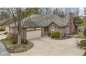 Charming brick home boasts an attached garage, mature landscaping, and concrete driveway on a sunny day at 2042 Oldfields Cir N Dr, Indianapolis, IN 46228