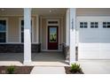 Inviting covered porch featuring stone accents, white columns, a brick facade, and bright red front door at 14383 Coyote Ridge Dr, Noblesville, IN 46060