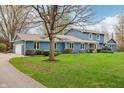 View of a blue house with a mature tree in the front yard, complemented by trimmed hedges and lush green grass at 1250 W 141St St, Carmel, IN 46032