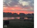 Stunning sunset over a serene pond in a residential community, captured behind a wrought iron fence at 6615 Aberdeen Dr, McCordsville, IN 46055