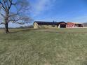 Scenic view of a ranch home surrounded by greenery, a large tree, and a red building in the background at 10966 W State Road 142, Quincy, IN 47456