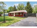A charming red home featuring mature trees, a well maintained lawn, and a paved driveway at 4754 E 64Th St, Indianapolis, IN 46220