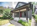 Charming home featuring a covered porch, gray siding, a red door, and lush landscaping at 615 E Morris St, Indianapolis, IN 46203