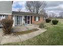Charming brick and vinyl exterior with a concrete patio, features a security door and mature shrubbery at 6808 Summer Time Dr, Indianapolis, IN 46226