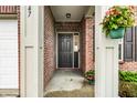 Inviting front porch featuring a decorative hanging plant and potted flowers, with a brick facade and classic black front door at 647 Albermarle Dr, Pittsboro, IN 46167