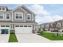View of townhome with gray siding, two-car garage, landscaping, and other homes in the distance at 1239 Newton St, Avon, IN 46123
