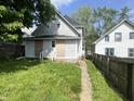 View of the backyard and exterior of a home, with an overgrown lawn and boarded up windows at 2148 Singleton St, Indianapolis, IN 46203