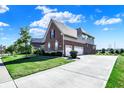 This two-story brick home has a three-car garage with a long concrete driveway, side-facing exterior, and manicured lawn at 3715 Kendall Wood Dr, Carmel, IN 46032