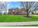 Stunning two-story brick home featuring a lush green lawn, mature trees, and a charming entryway at 13225 Snow Owl Dr, Carmel, IN 46033