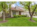 Charming home with well-manicured lawn and beautiful tree features a stone chimney and vibrant red door at 6404 Bayside Ct, Indianapolis, IN 46250