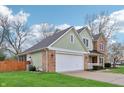 A view of the green and brick exterior, attached garage, and well-maintained lawn of this two-story home at 11117 Harriston Dr, Fishers, IN 46037