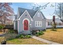 View of charming gray home with a red arched entry door, gray roof, and traditional lawn with spring color at 2309 Pearl St, Columbus, IN 47201